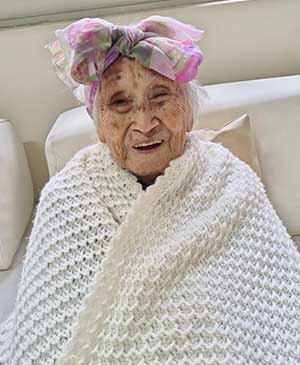 imagem de uma senhora rindo com um cobertor branco e um lenço na cabeça florido na casa de repouso mamma mia
