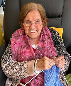 imagem de uma senhora no sofá tricotando uma roupa azul na casa de repouso mamma mia